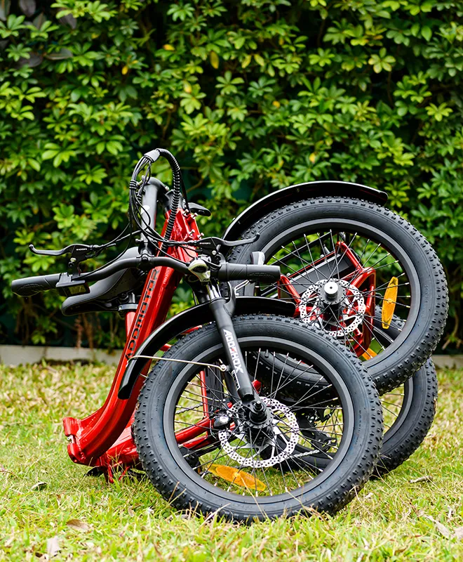 a red tricycle with 3 wheels is folded on the grass with a lot of leaves at the back