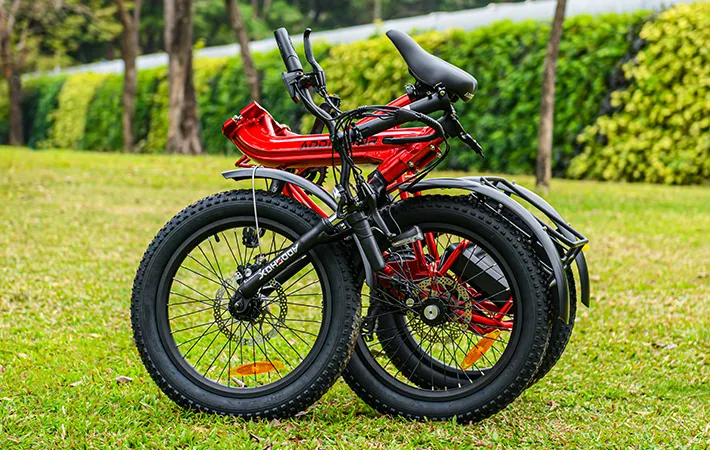 a foldable and light-weight folding etrike citytan in red is foloded on the grass in a park 