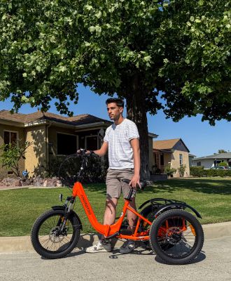 A man stands next to an orange electric trike on a suburban street